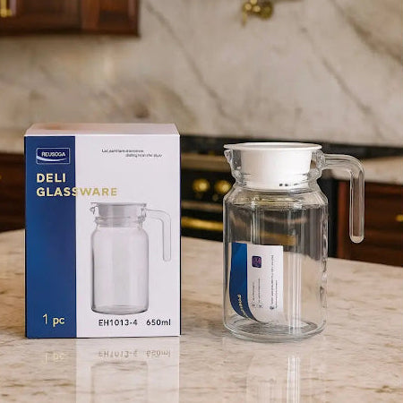 Clear glass pitcher with handle next to its packaging on a marble countertop